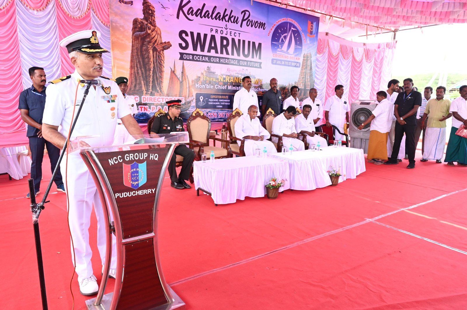 Naval officer addressing the ceremony beneath the Kadalakku Povom · Project SWARNUM banner